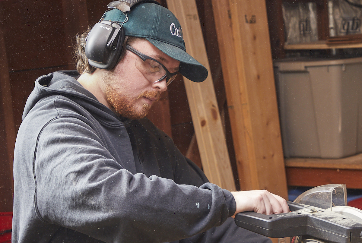 Man using a miter saw wearing safety glasses and hearing protection.