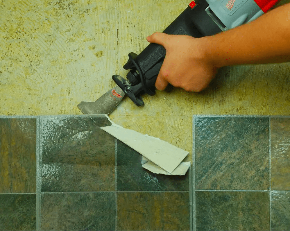 Person uses an attachment on a reciprocating saw to peel the adhesive backing off the back of adhesive tile.