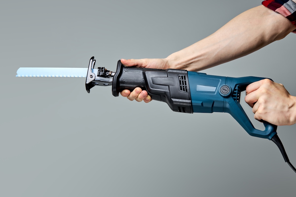 Reciprocating saw used in construction and demolition work, in male hands. copy space