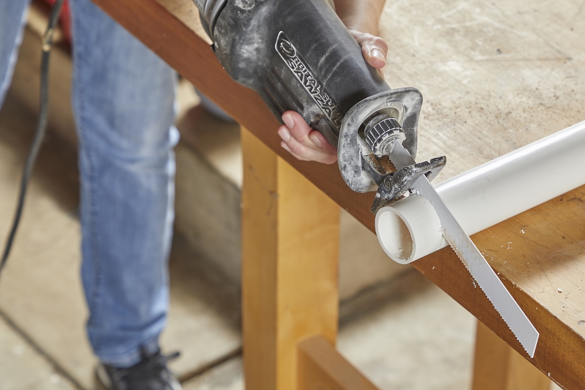 Woman uses a reciprocating saw to cut through PVC pipe.