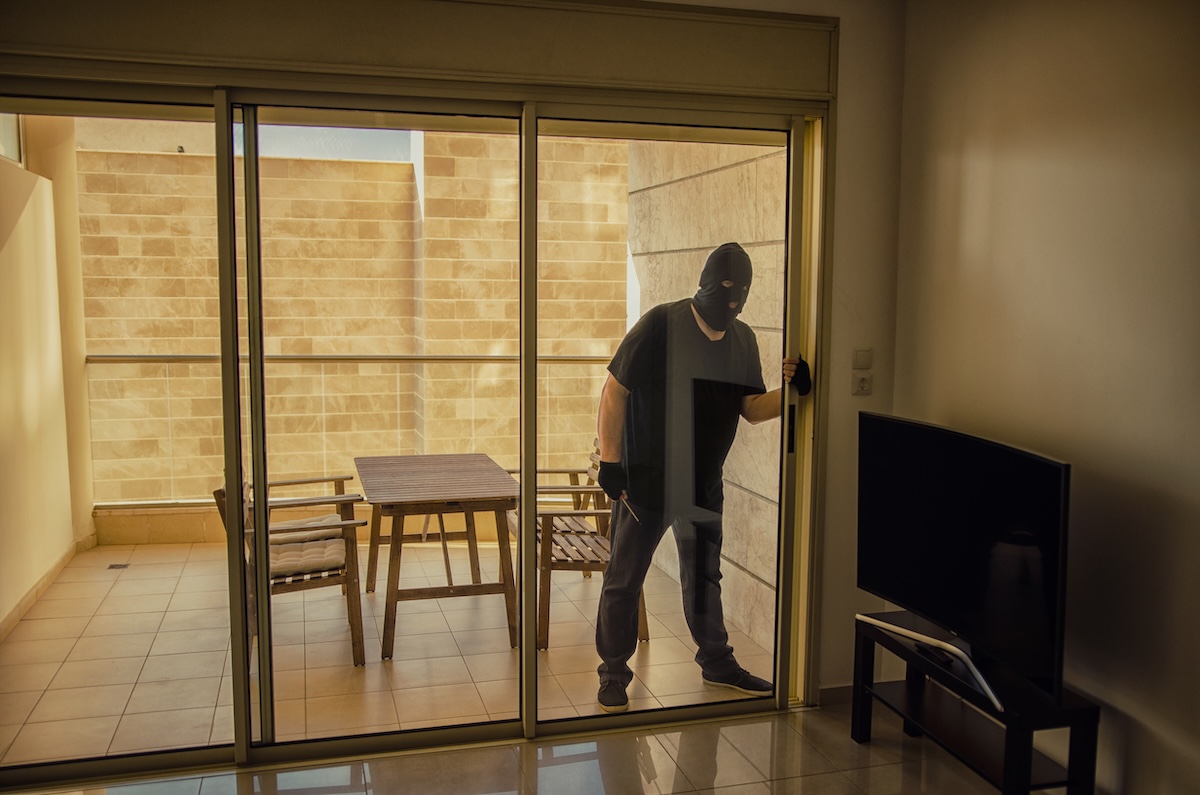 A thief peers through a sliding glass door where a television sits inside.