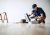 A worker crouching over an open toolbox in an empty room.