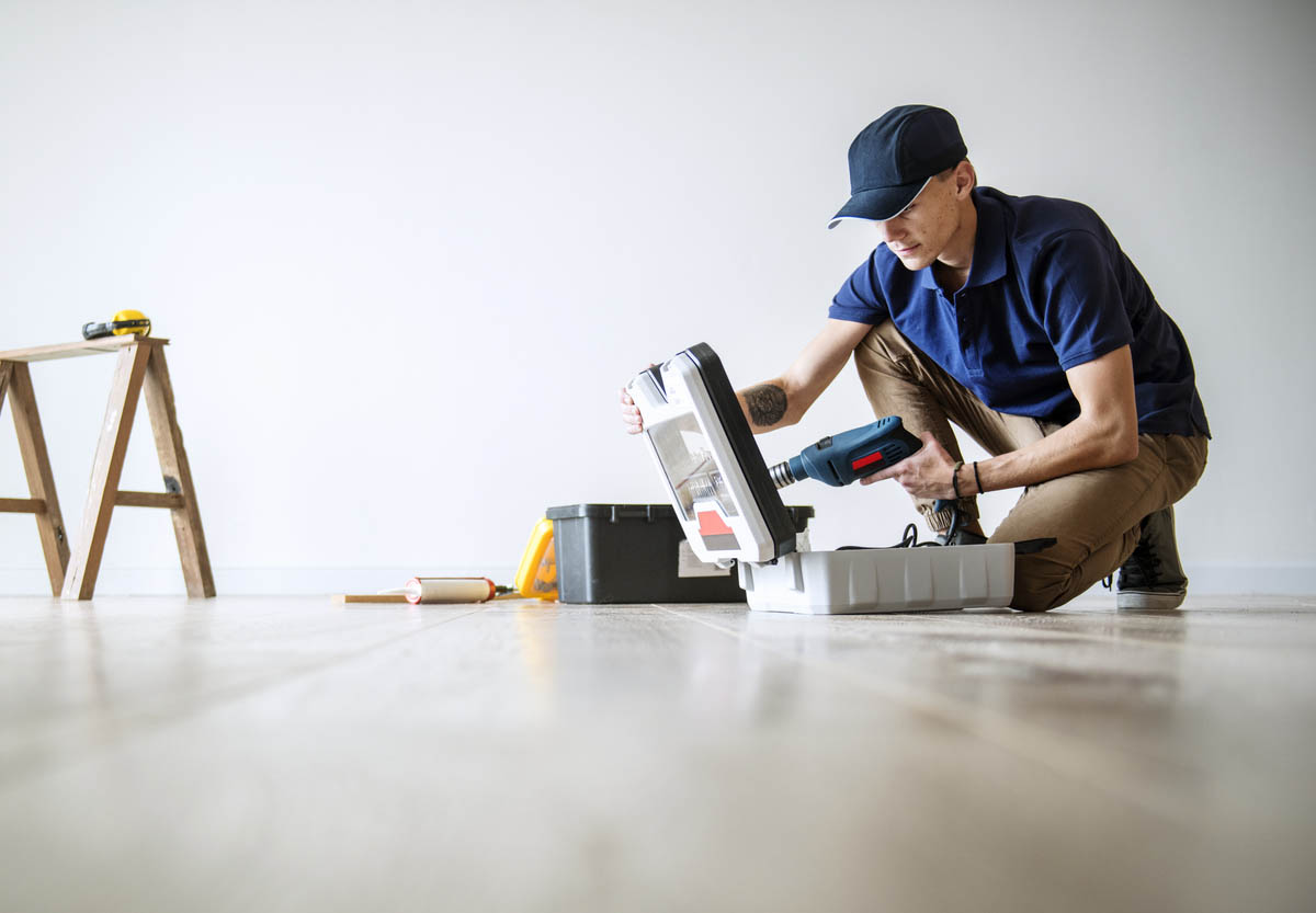 A worker crouching over an open toolbox in an empty room.