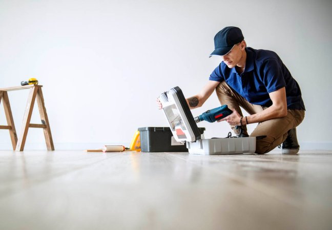 A worker crouching over an open toolbox in an empty room.