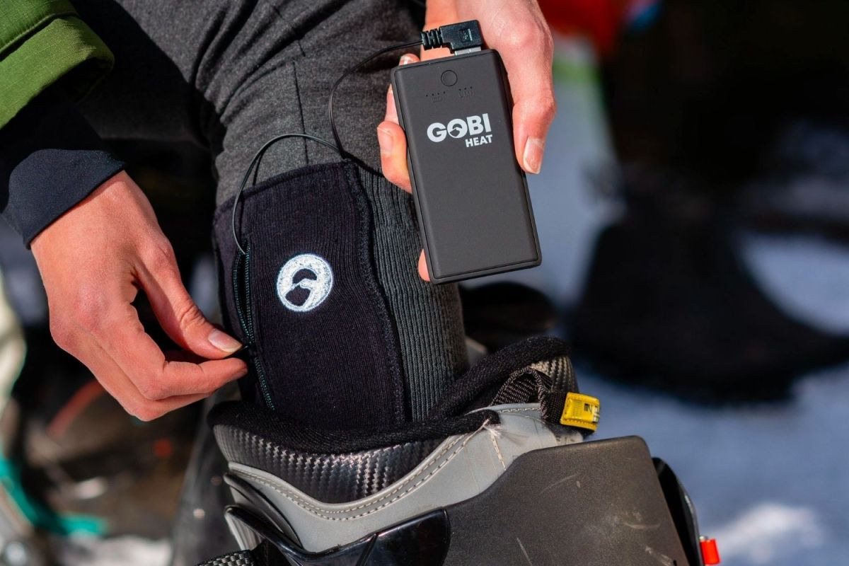 A person using a remote to adjust the best heated socks while their foot is in a ski boot.