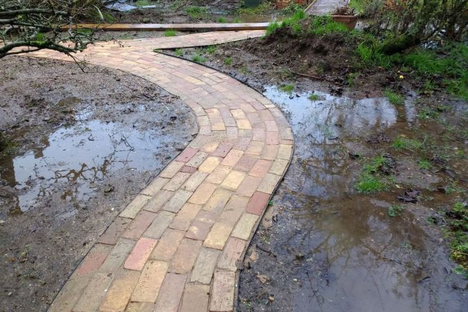A view of a wet and soggy yard and paved pathway.