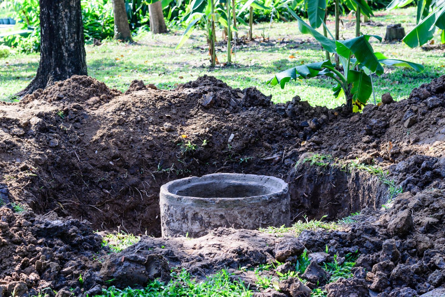 A drain is exposed in a hole in a yard.