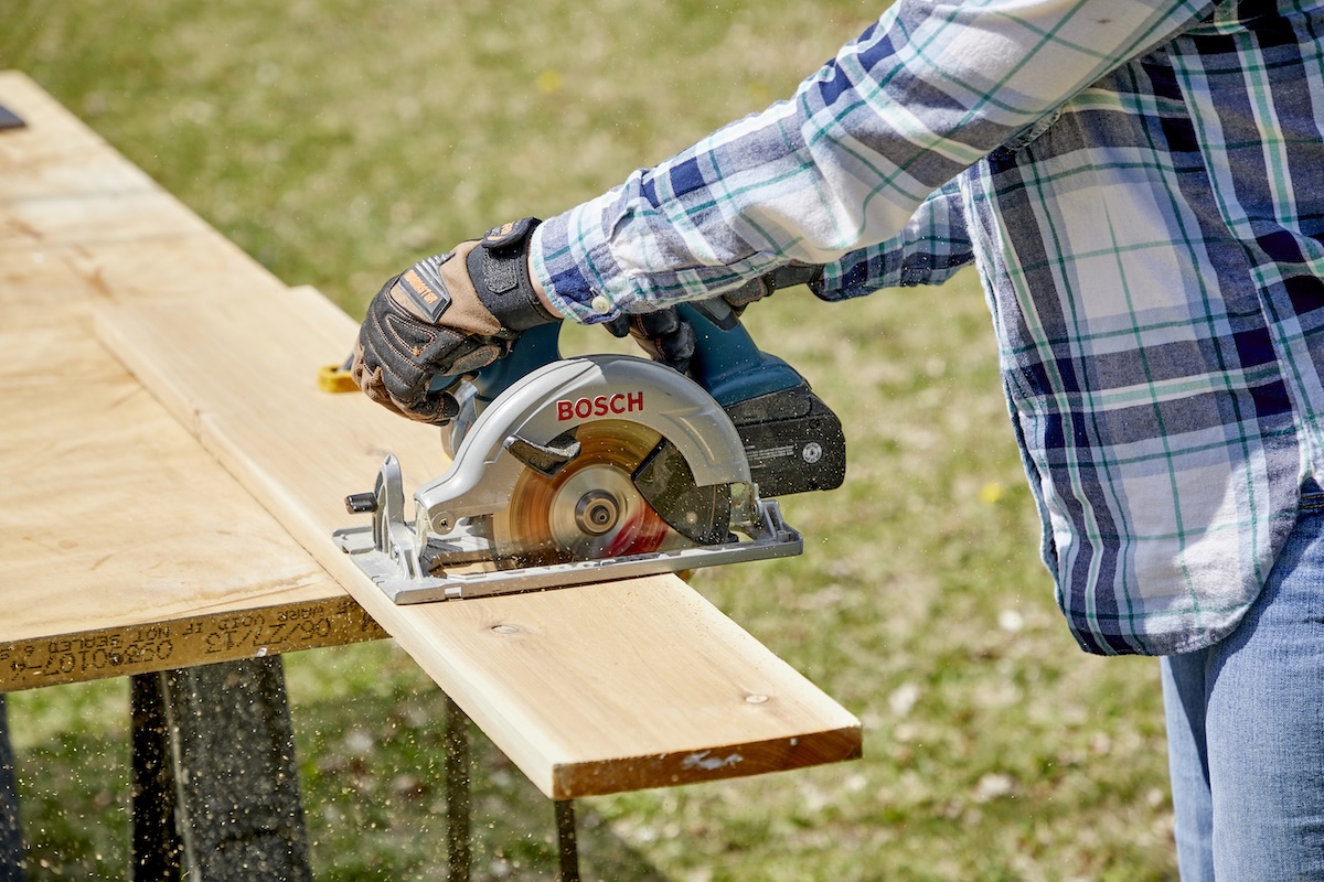 Woman uses a circular saw to cut a piece of lumber.