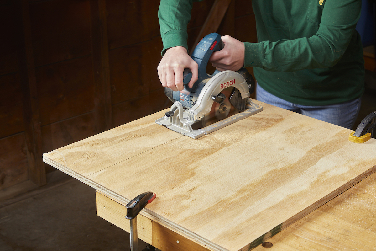 Woman uses a circular saw to cut along a marked line on plywood.