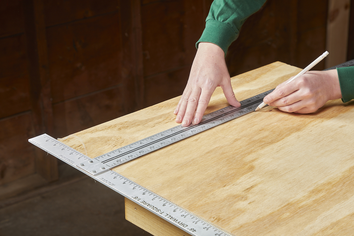 Woman measures and marks a board of plywood.
