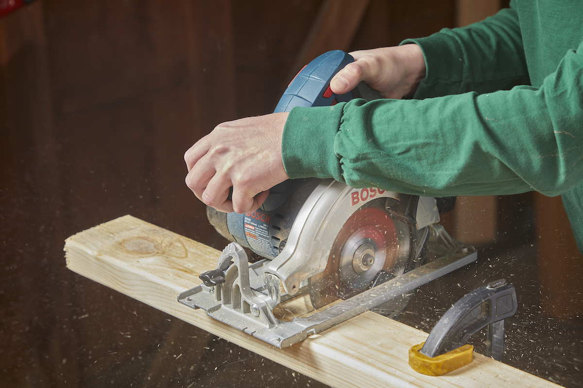 A circular saw is cutting a 2x4., guided by a woman's hands.