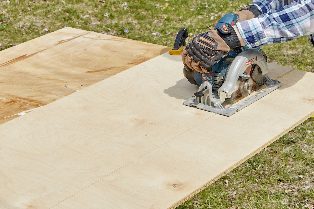 Woman uses a circular saw to cut a large piece of plywood.