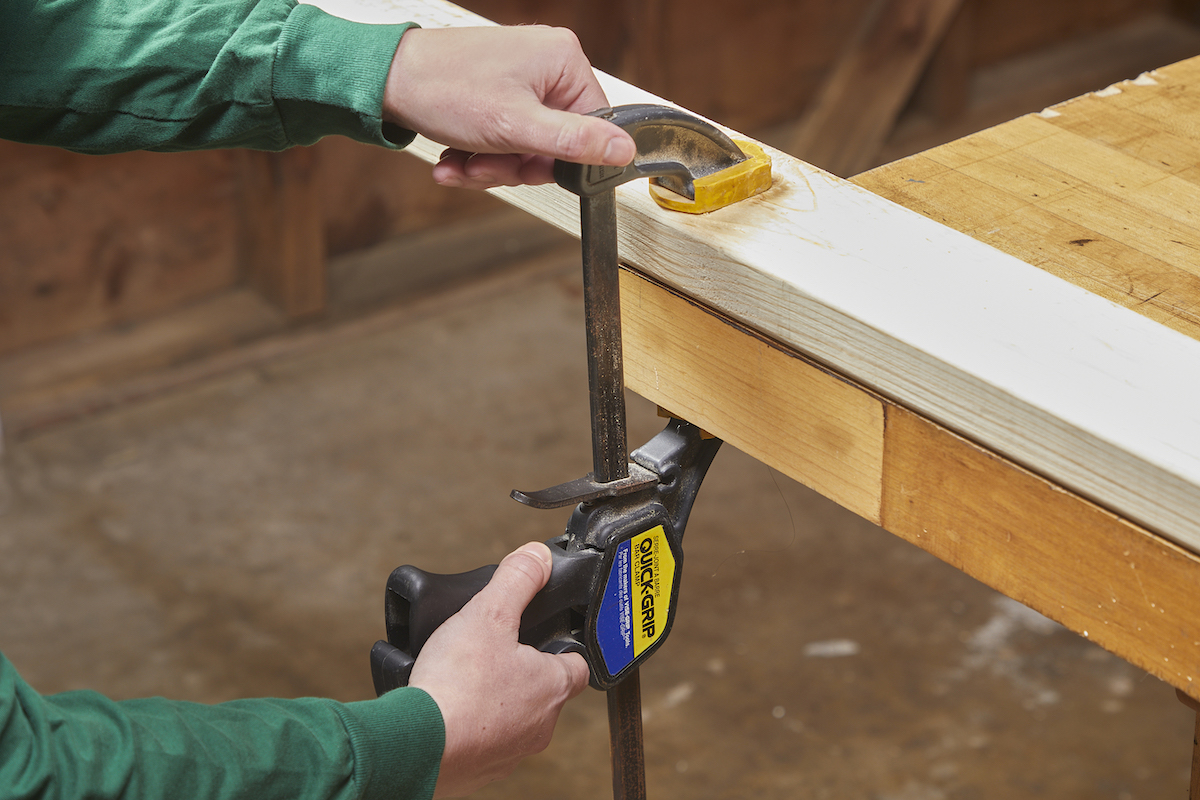 Woman clamping a 2x4 to a work table before cutting it with a circular saw.