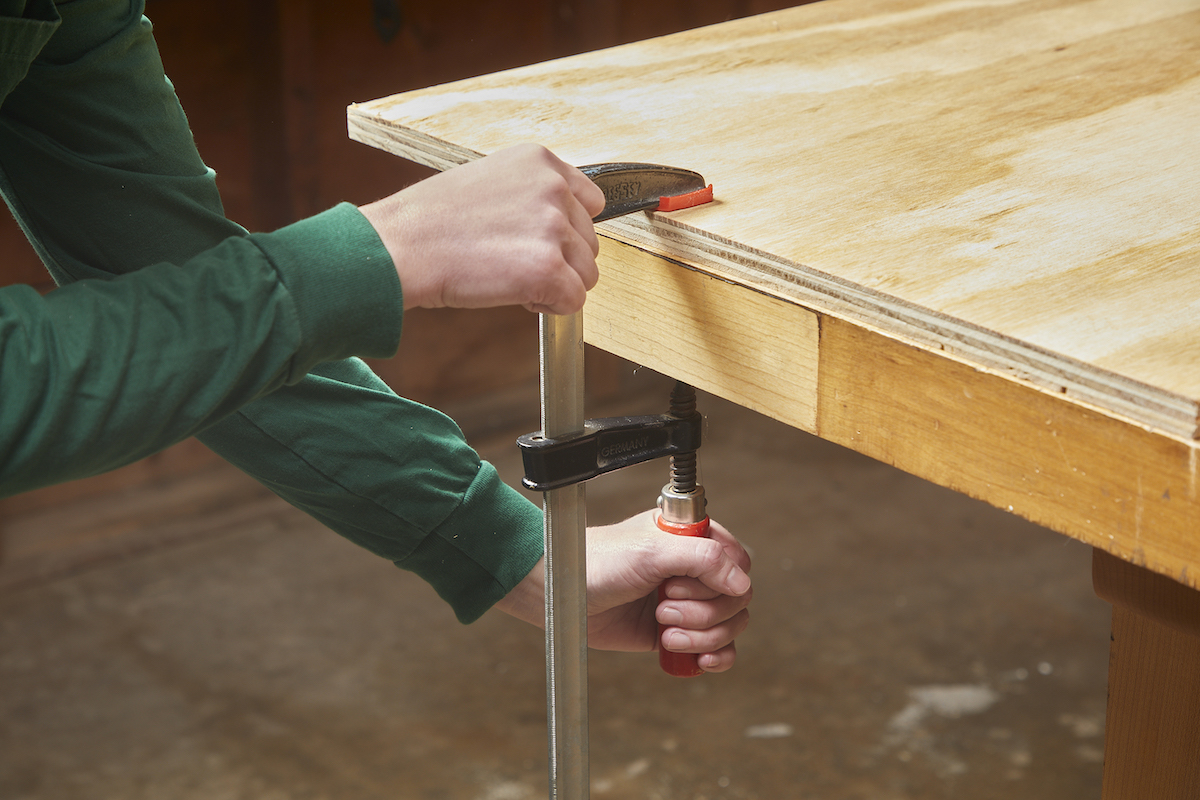 Woman uses clamp to attach plywood to work table.