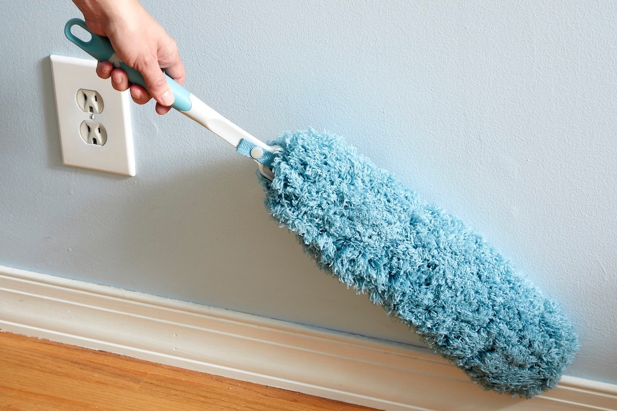 Woman uses a microfiber duster to clean baseboards before applying painter's tape.