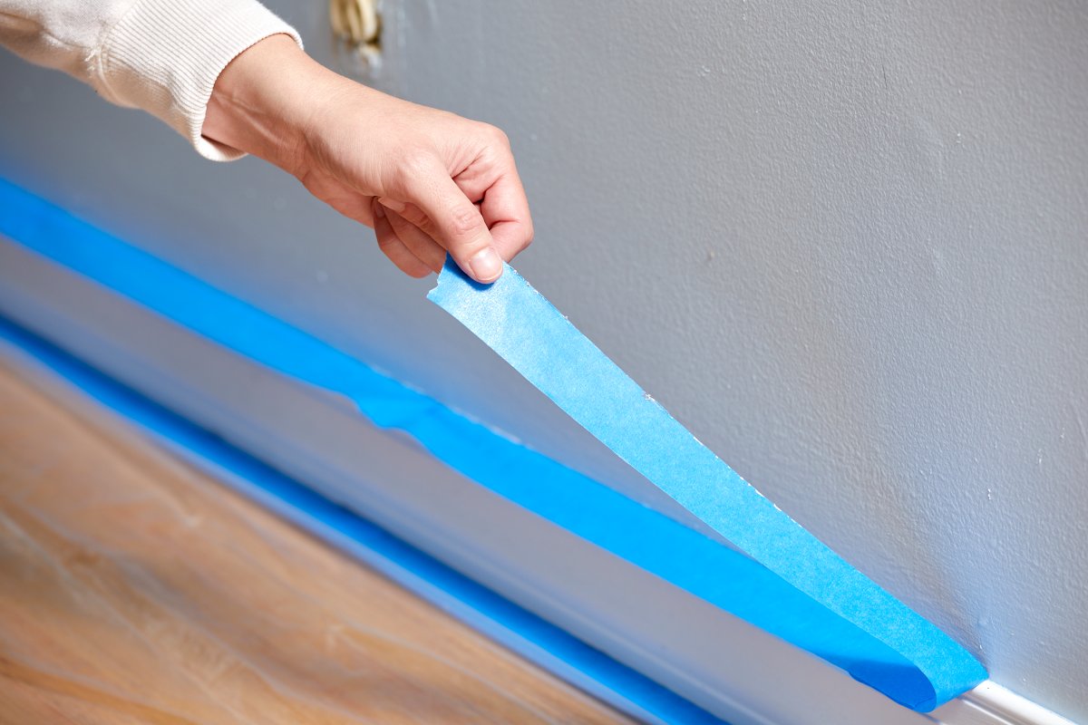 Woman pulls painter's tape off a baseboard.