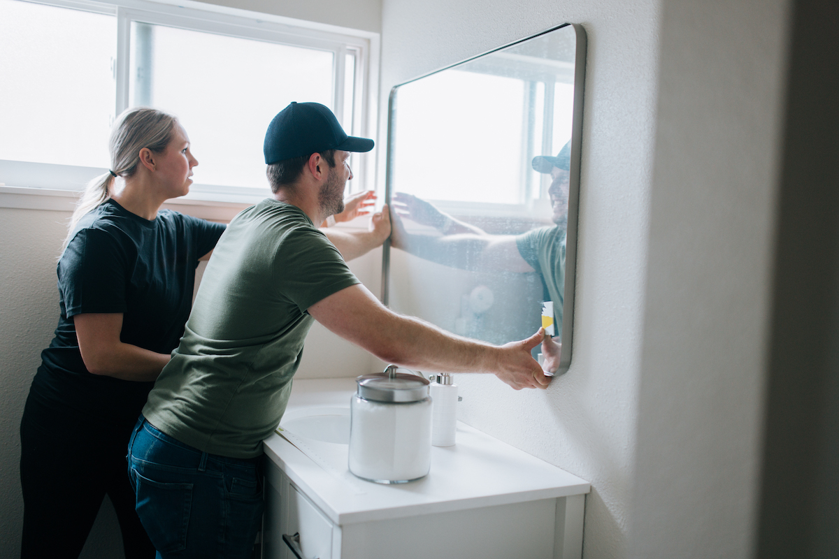 A Caucasian couple install a bathroom mirror in their house for a renovation project.