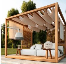 Gorgeous pergola with a white puffy couch underneath, and white cloth hanging from the slats overhead.