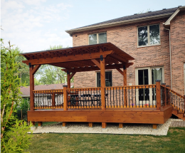 Deck-pergola combination in wood attached to a brick house.