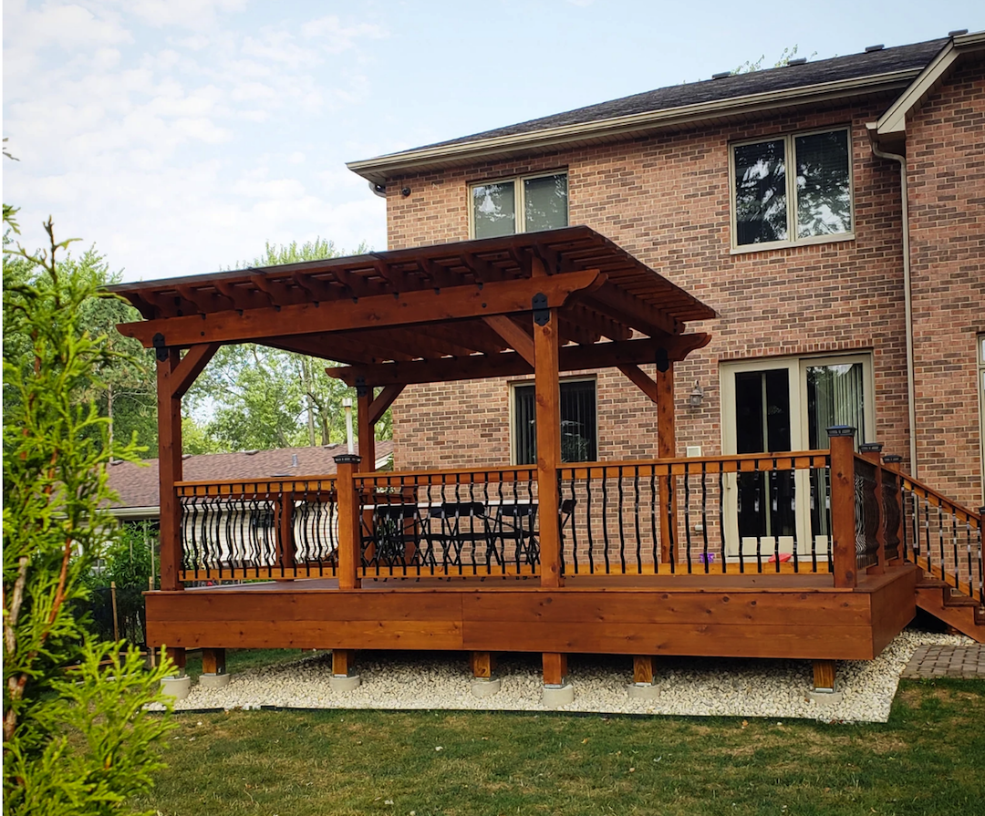 Deck-pergola combination in wood attached to a brick house.