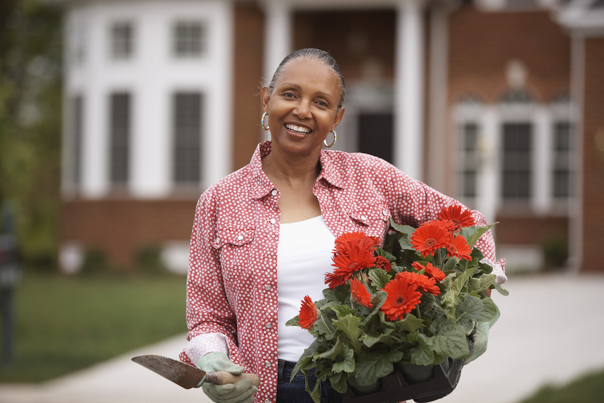 Woman holding a red flowering plant in her driveway.