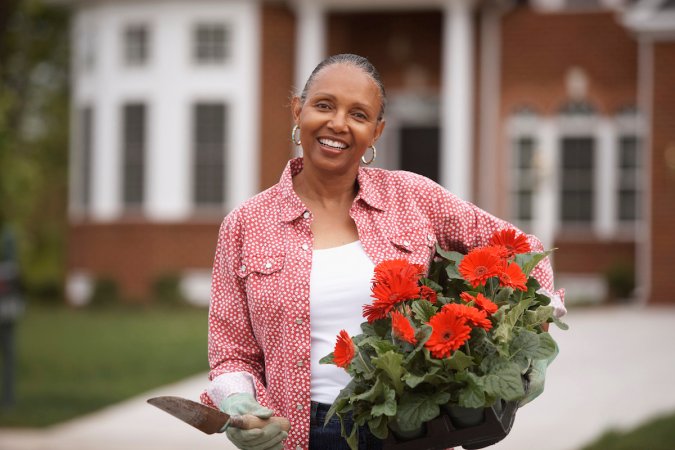 Woman holding a red flowering plant in her driveway.