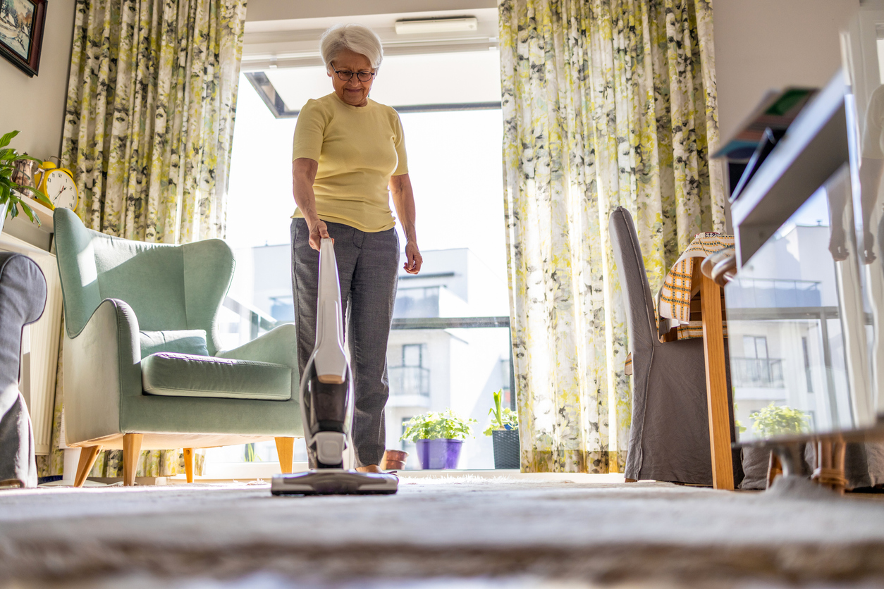A senior using the best lightweight vacuum for seniors to clean a rug in a bright living room.