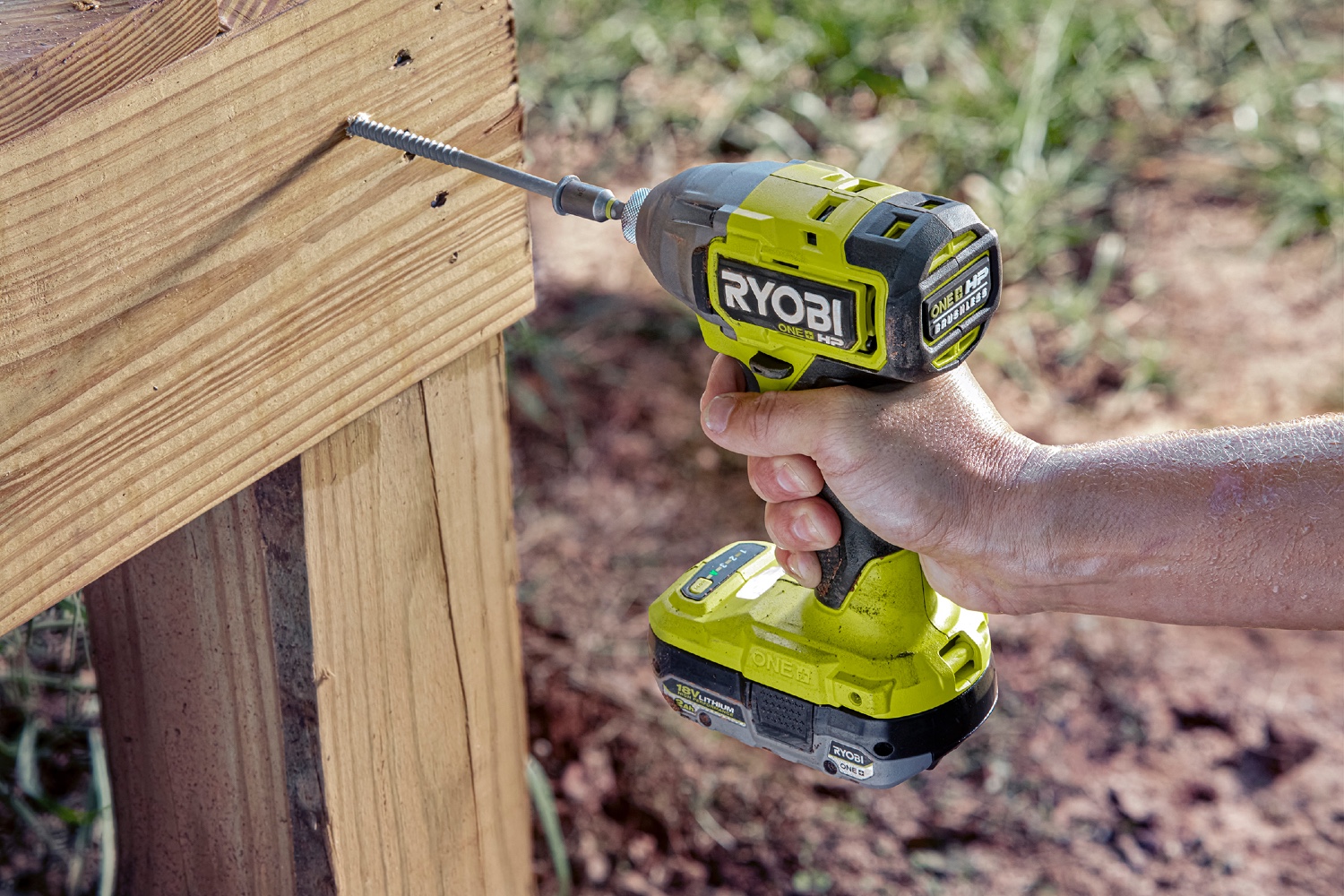 A person using the best Ryobi drill to drive a large screw into an outdoor wooden structure.