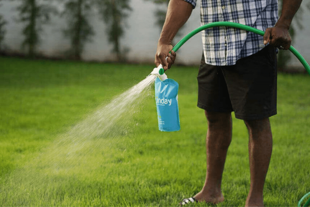 A person is shown spraying a Sunday lawn care product on their lush, green lawn.