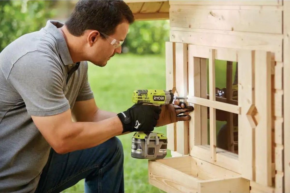 A person using the best Ryobi drill to build a wooden playhouse outdoors.