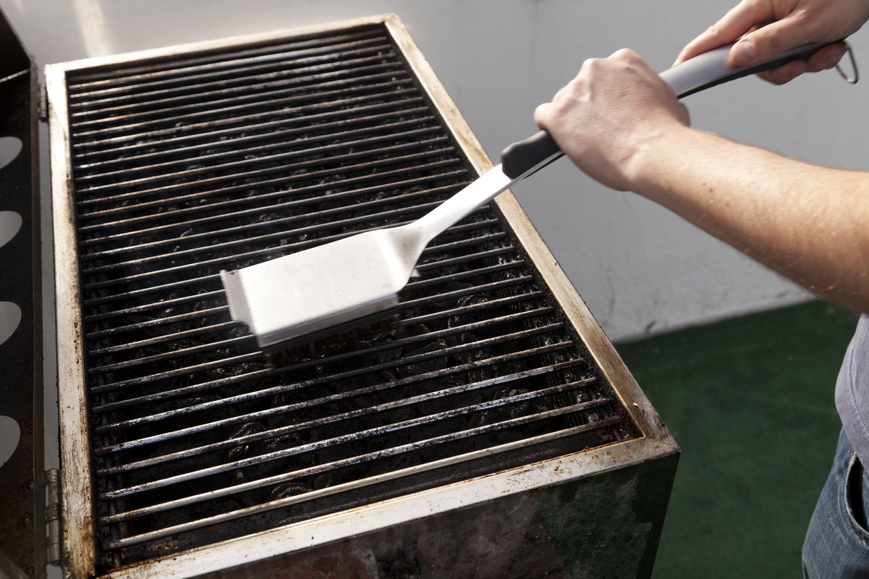 Person using a grill brush to clean dirty grates on a grill.