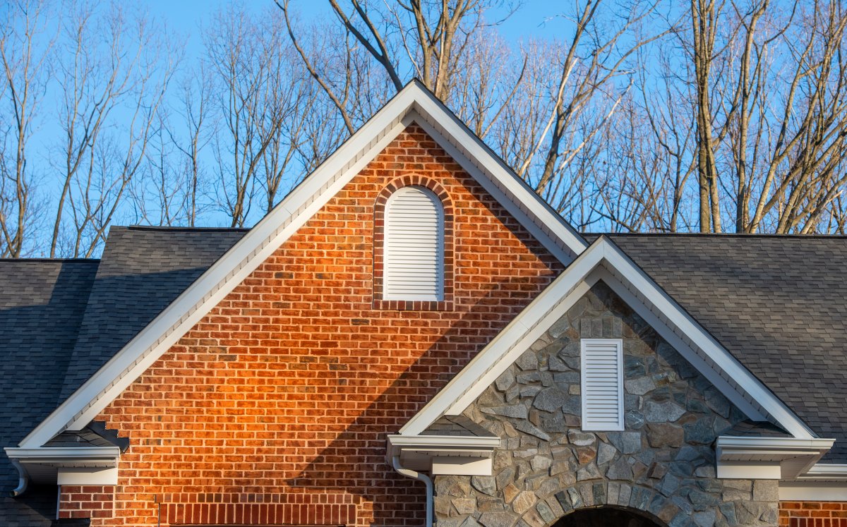 Colonial white round top and vertical gable vents on a brick and stone veneer facade double peak gabled home.