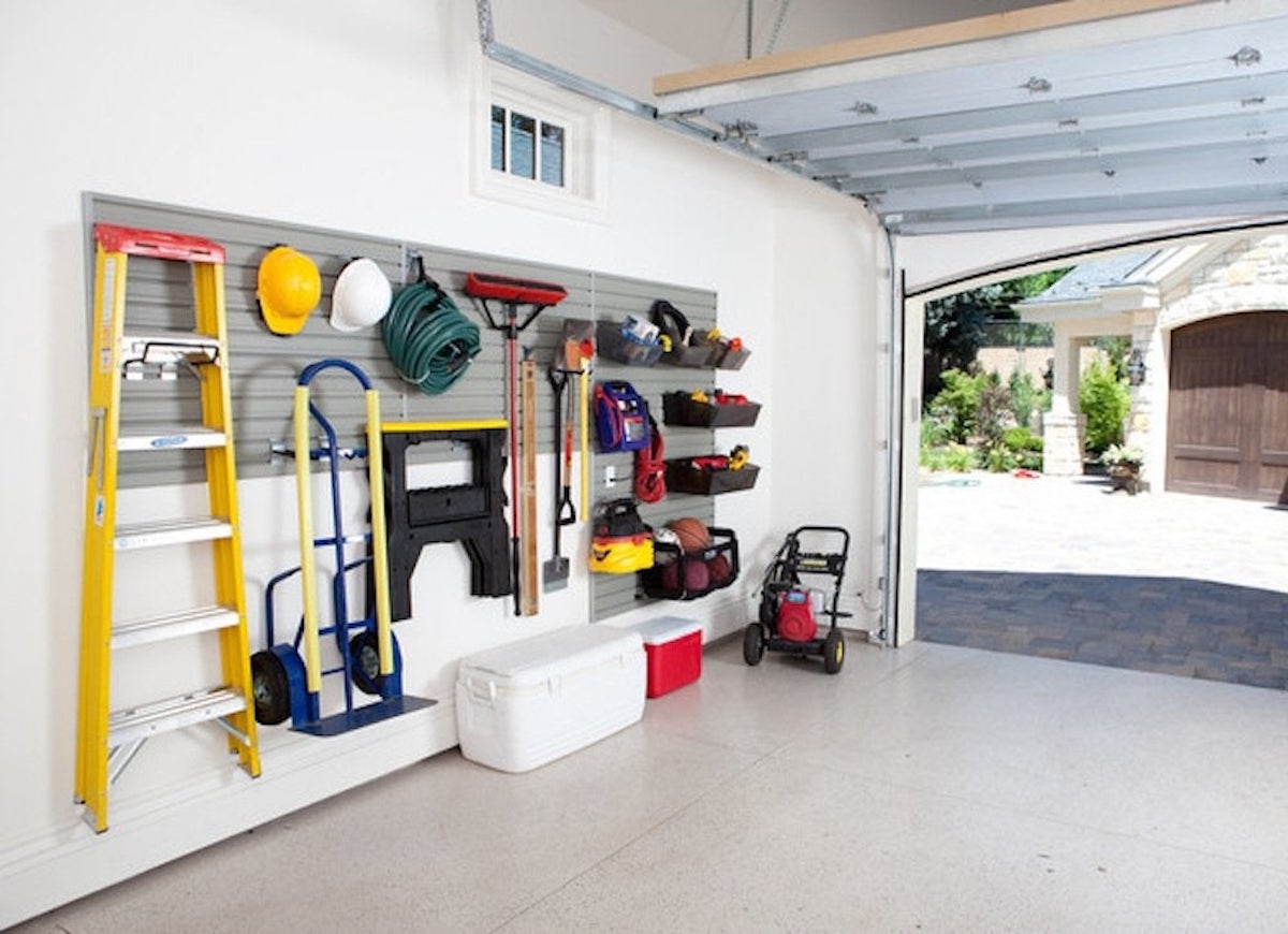 A clean, organized garage with a ladder and other supplies hanging on a wall organizer.