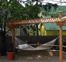 Backyard scene with a hammock hanging from a wood pergola.