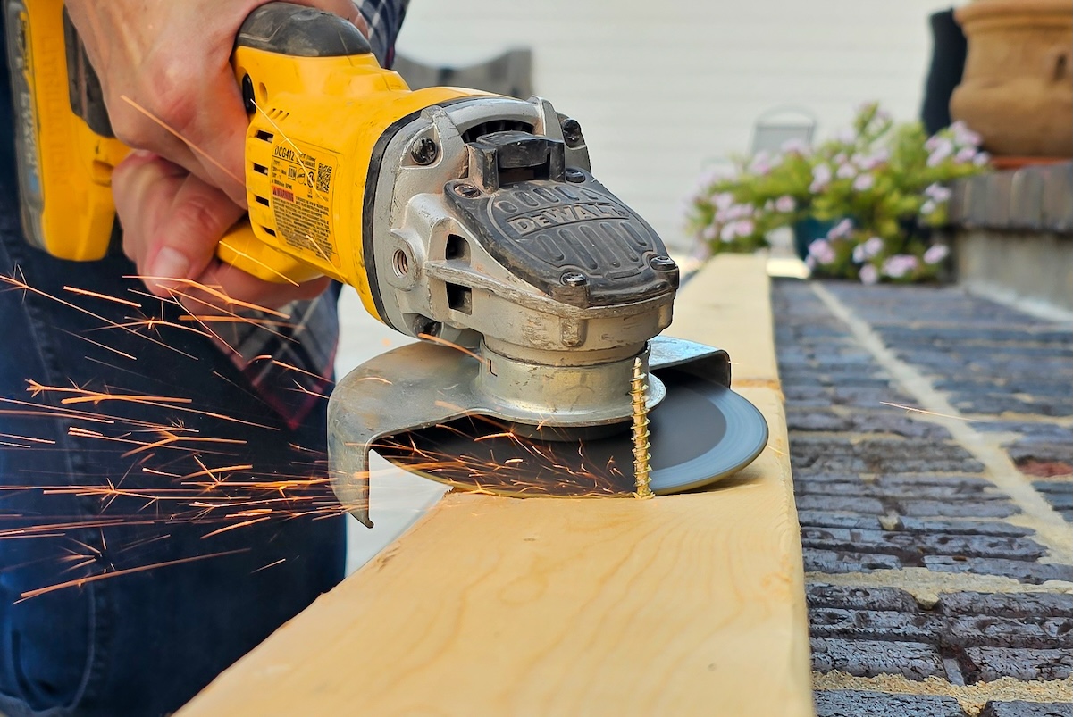Person uses an angle grinder to cut a screw in a piece of wood.