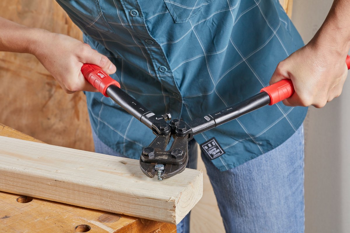 Woman uses bolt cutters to clip screw out of a piece of wood.