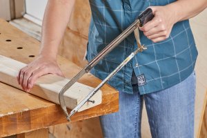 Woman uses hacksaw to cut screw out of piece of lumber.