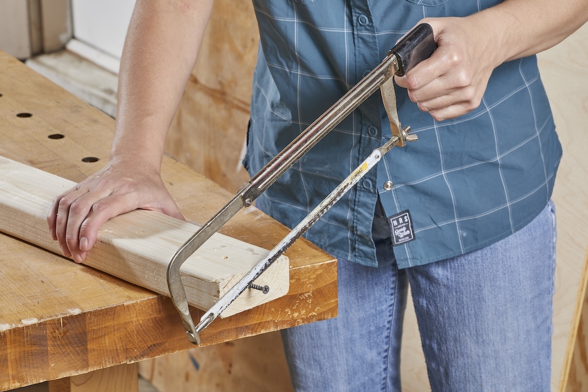 Woman uses hacksaw to cut screw out of piece of lumber.