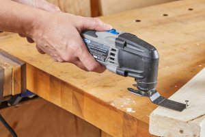 Person uses oscillating tool to cut screw out of wood.