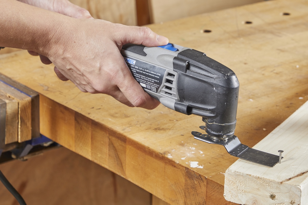 Person uses oscillating tool to cut screw out of wood.
