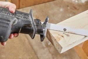 Person uses a reciprocating saw to cut through a screw in a piece of wood.