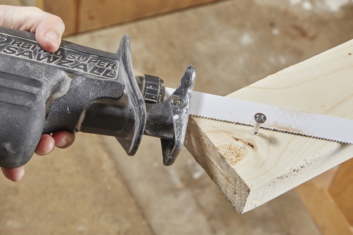 Person uses a reciprocating saw to cut through a screw in a piece of wood.