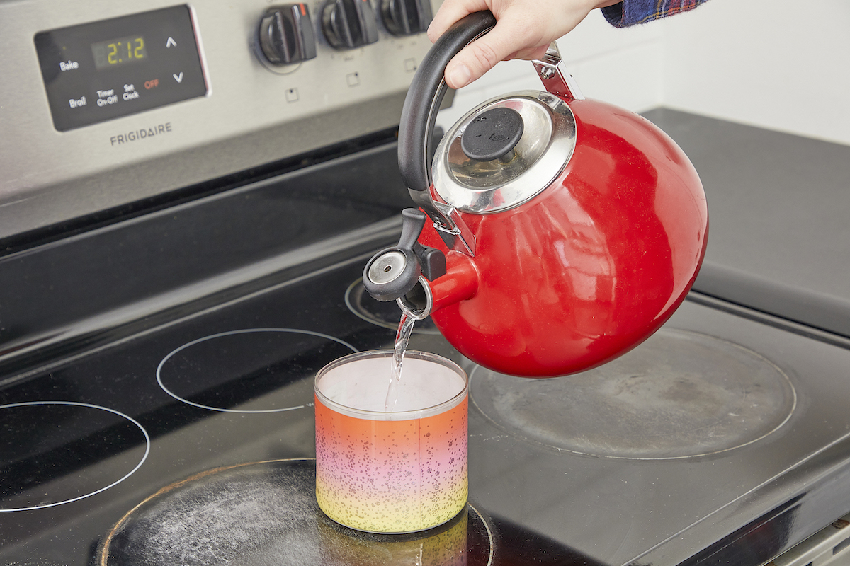 Woman pouring boiling water from red tea kettle into a candle jar.