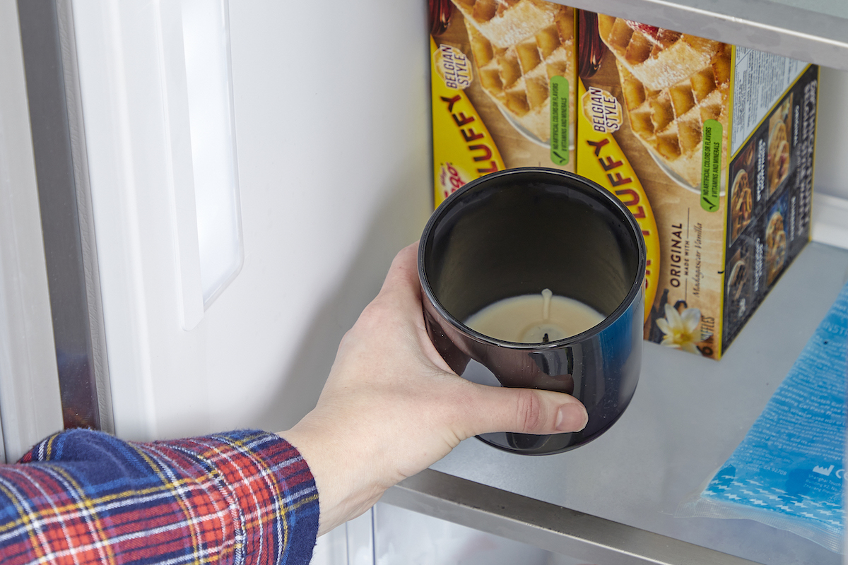 Woman puts candle in black jar into freezer in front of frozen waffles.