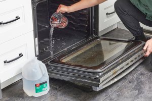 Woman pours measuring cup of distilled water onto bottom of oven.