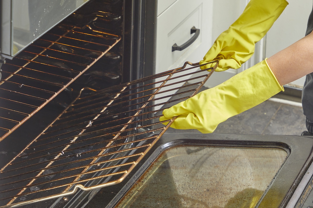 Woman wearing rubber cleaning gloves removes racks from an oven.
