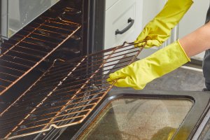 Woman wearing rubber cleaning gloves removes racks from an oven.