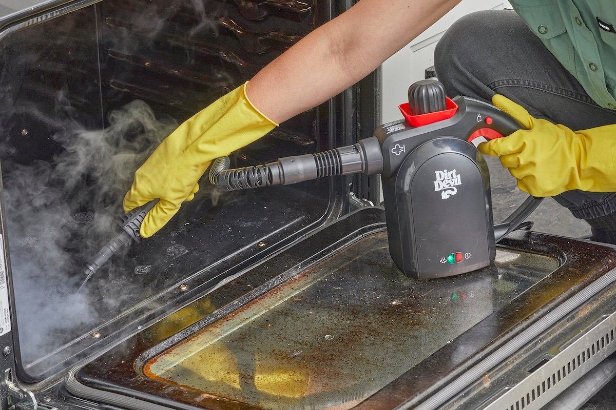 Woman uses steam cleaner to clean the interior of an oven.