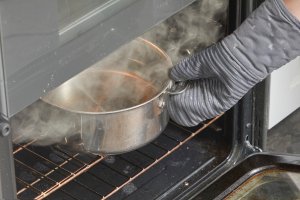 Person pulls steaming stainless pot of water out of an oven.
