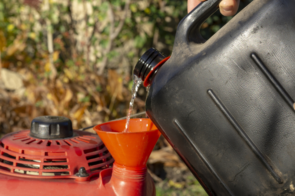 Person pours gas from gas can into lawn mower gas tank.